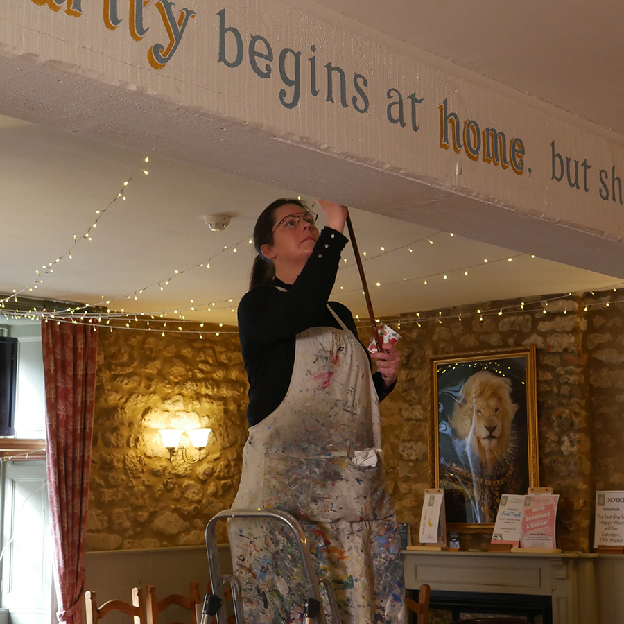 Artist Jemma Thompson working on painting local sayings onto walls of the White Lion community pub in Broadwindsor